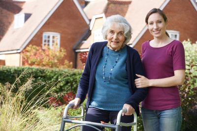 caregiver helping senior woman to use walking frame